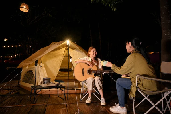 Two beautiful young Asian female friends enjoy camping at night together in the campground. Outdoor activity concept