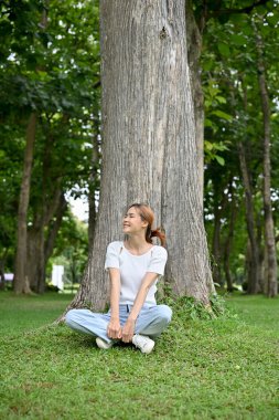 Güzel ve neşeli Asyalı kadın güzel yeşil bahçedeki büyük ağacın altında oturuyor..