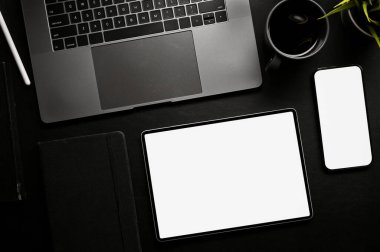 Modern black office desk workspace with opened notebook laptop, coffee cup, smartphone and digital tablet white screen mockup. top view, flat lay