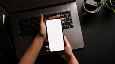 Modern siyah ofis çalışma alanı üzerinde akıllı telefon beyaz ekran maketi tutan bir kadın el. Üst görünüm