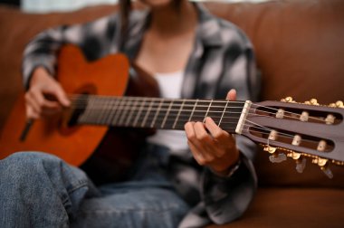 A talented millennial Asian female relaxes in her living room and plays her acoustic guitar. cropped and close-up image