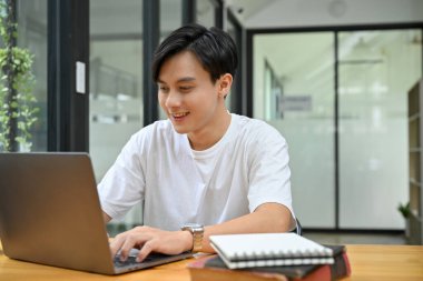 Smart and handsome young Asian male office worker or tech engineer working at his office desk, using laptop computer.