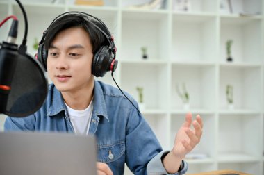 Handsome and talented young Asian male freelance podcast radio host running his show, using headphones and microphone. Podcast concept