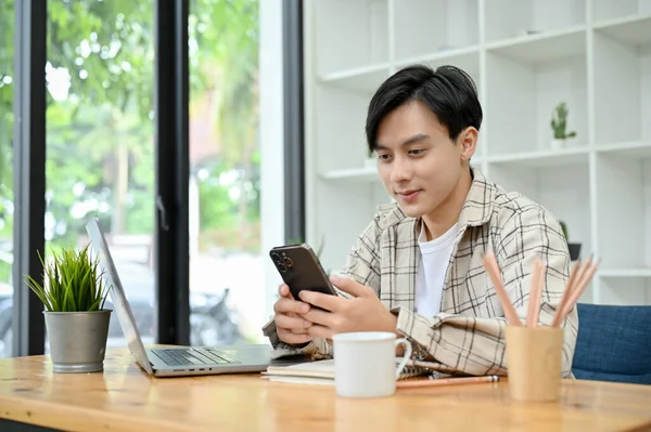 Cheerful Millennial Asian Male His Office Desk Workspace Using Smartphone — Foto de Stock