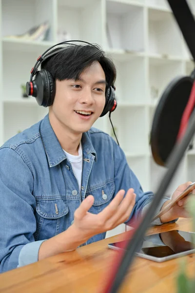 Portrait, Cheerful and happy young Asian male podcaster or online radio host in his studio, enjoys talking with his guest from the call. Podcast content
