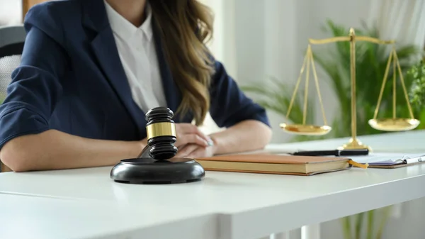 Professional female lawyer or business legal consultant in formal suit sits at her office desk with judge gavel and scales of justice are on her office desk. cropped image