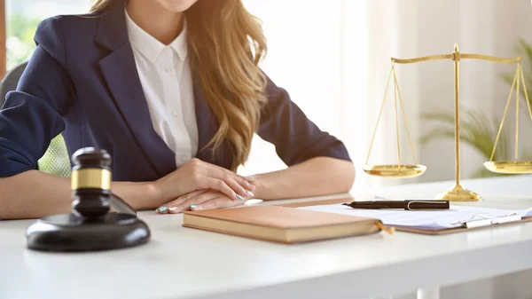 A professional and successful female lawyer or business legal consultant in formal suit sits at her office desk. Judge gavel and scales of justice are on the table. cropped and close-up image.