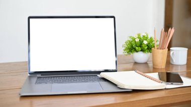 Workspace with notebook laptop computer white screen mockup, spiral notebook, smartphone, stationery and decor on wood table. close-up image