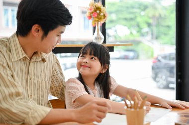 Proud dad and cute little girl smiling and looking each other in the eye while playing and painting together.