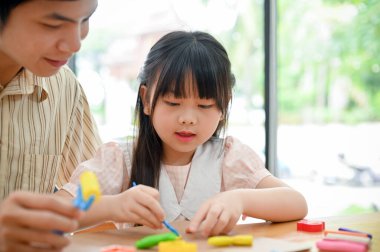 An adorable young Asian girl concentrating learning and sculpting play dough with her dad. Plasticine, Clay or Play dough.