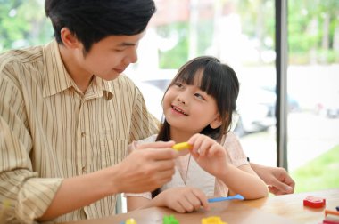Lovely and smiling young Asian girl enjoys playing play dough or plasticine with her dad. Creative kids activity concept