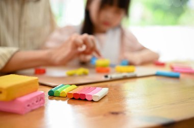 Colorful plasticine or play dough on a table over blurred background of dad and daughter playing and moulding play dough together. cropped and close-up image