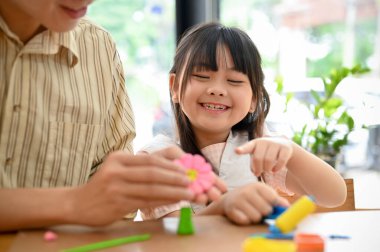 Cute little Asian girl have a fun time with her dad, doing creative activity together, moulding colorful clay or play dough.