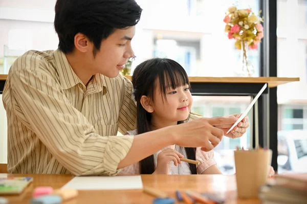 Proud and kind Asian dad showing and teaching how to paint and draw a cute animal on a paper to his daughter. Lovely family concept