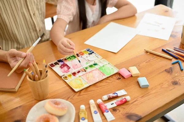 An Asian dad and daughter painting with a watercolor together at home. Happy family time, fun creative activity for kids. cropped and above view image