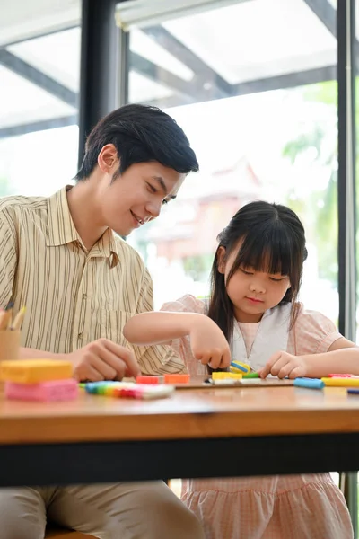 Portrait, A happy young Asian girl concentrates and enjoys sculpting play dough, moulding clay, and playing play dough with her art teacher.