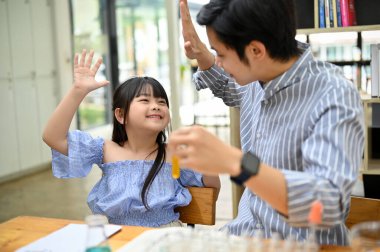 Happy proud dad or teacher giving high five to his cute little girl, doing fun science experiment for kids. enjoying learning and doing fun activity together.