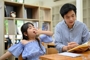 Pretty and charming young Asian girl yawning while her private tutor teaching math in the cafe. kindergarten or primary school kids.