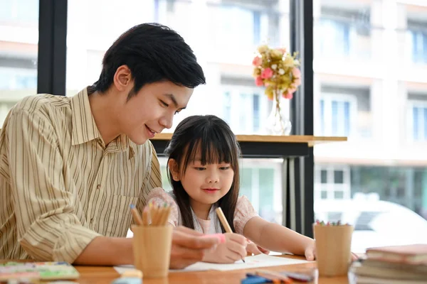 Cheerful Asian male art teacher is teaching and showing how to draw cute animals to his young female student. Kids with Art concept