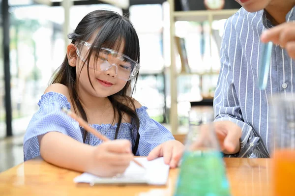 Cute Young Asian Girl Science Goggles Taking Notes Her Notebook — Stockfoto