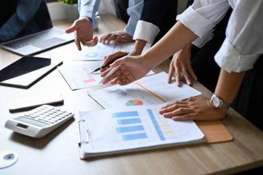 Professional Asian businesspeople analyzing financial and marketing data on the report together in the meeting. cropped image