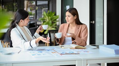 İki mutlu ve neşeli Asyalı genç iş kadını ya da bayan iş arkadaşı ofiste kahve molası sırasında sohbet etmekten ve birlikte kahve içmekten zevk alırlar.. 