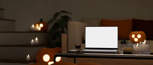 Modern living room in Halloween night with portable laptop white screen mockup and Halloween decor on coffee table. Dark workspace at night. 3d rendering, 3d illustration