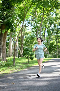 Portre, sağlıklı formda spor giyimli Asyalı kadın yeşil şehir parkında koşuyor veya koşuyor..