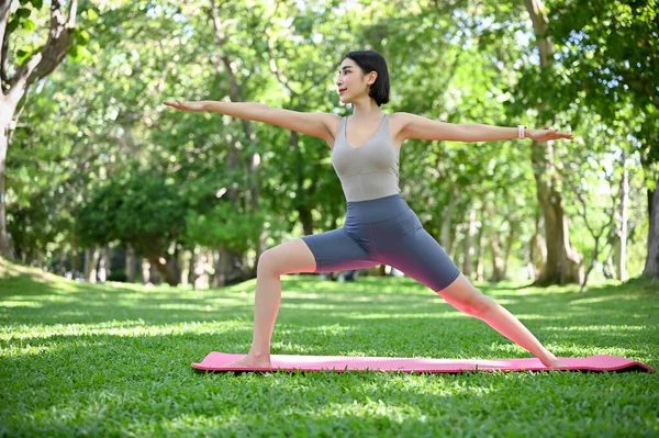 迷人的适合亚洲女人穿着时髦的运动服练习瑜伽 站在公园里的瑜伽垫上做一个练习 健康和福利概念 — 图库照片