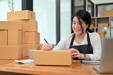 Güzel genç Asyalı kadın e-ticaret girişimi girişimcisi nakliye paketlerini ofiste hazırlıyor..