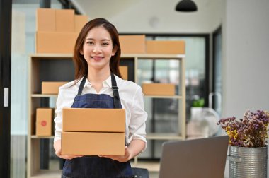 Gülümseyen Asyalı genç bir kadın e-ticaret işadamı elinde karton kutular ya da depoda tutuyor. Çevrimiçi iş kavramı.
