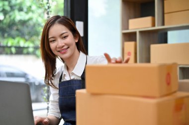 Çekici ve mutlu Asyalı genç bayan e-ticaret girişimcisi ofisteki nakliye paketlerini kontrol ediyor. Çevrimiçi alışveriş konsepti.