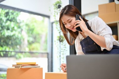 Güzel ve meşgul Asyalı genç bayan girişimci tedarikçisiyle telefonda konuşurken ofiste bir nakliye siparişi hazırlıyor..