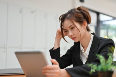Düşünceli genç Asyalı iş kadını tablet kullanıyor, bir iş stratejisi düşünüyor ve projesine konsantre oluyor..