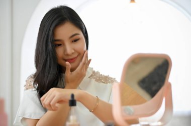 Kendine güvenen ve zarif Asyalı bayan güzellik blogcusu cilt bakım serumunu yüzüne uyguluyor..