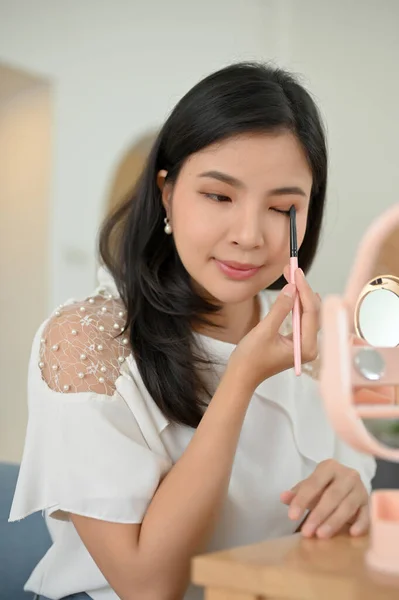 Portrait, Charming asian female makeup artist holding an eyeshadow palette, applying a beautiful eyeshadow on her eyelid with makeup brush. beauty concept