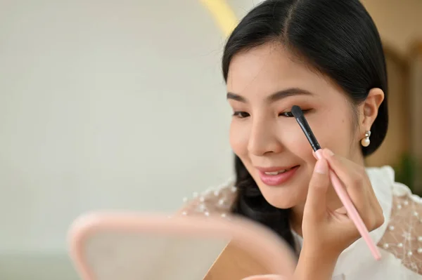 Beautiful and charming asian female makeup artist holding an eyeshadow palette, applying a beautiful eyeshadow on her eyelid.