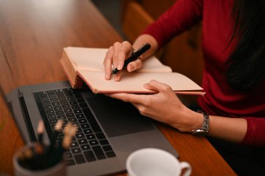 A professional businesswoman is listing something on her notebook while working at her office desk. cropped and close-up image