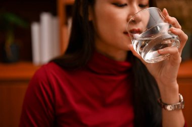 Beautiful calm millennial Asian female or businesswoman drinking water while working in her private office. close-up image