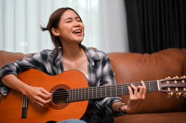 Talented and attractive young Asian female sings her favourite song while playing an acoustic guitar. Hobby and lifestyle concept