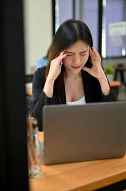 Portre, stresli ve yorgun Asyalı genç iş kadını ofis masasında oturuyor, yorgun, başı ağrıyor ya da işi yüzünden üzgün..