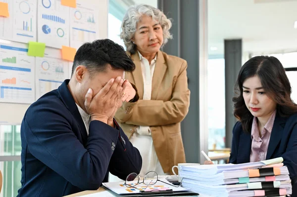 Sad and stressed Asian male office worker or businessman receives a complaint from his boss while working on his project with his team.