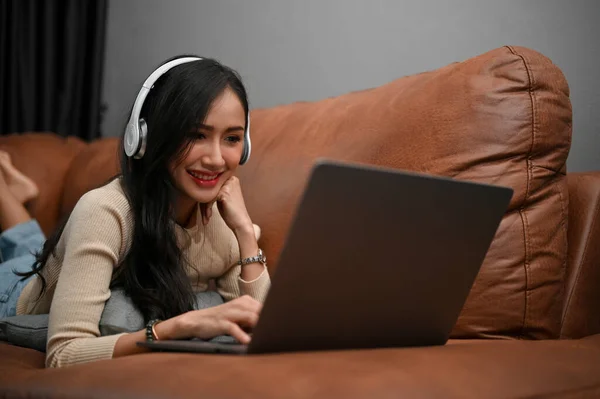 아름다운 아시아 양귀비 소파에 헤드폰을 노트북으로 영화를 있습니다 취미와 — 스톡 사진
