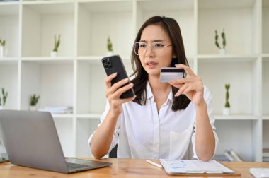 Milenyum Asyalı mutsuz ve kafası karışmış bir kadının cep telefonu ve kredi kartı ile masasında otururken cep telefonu başvurusunda bir sorunu var..