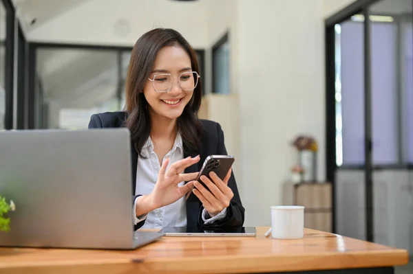 Güzel ve çekici Asyalı iş kadını, gözlüklü, masasında akıllı telefonunu kullanarak bir müşteriye e-posta ya da sohbet yolluyor..