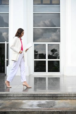Portre, çekici ve zarif bin yıllık iş kadını ya da beyaz takım elbiseli kadın yönetici bina boyunca yürüyor..