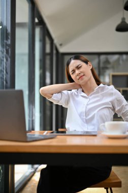 Yorgun, yorgun ve çok çalışan Asyalı genç iş kadını ya da masasında çalışan kadın boyun ağrısı ya da ofis sendromu çekiyor..