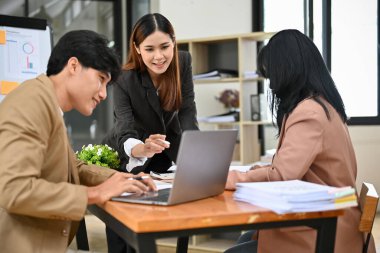 Profesyonel ve çekici Asyalı bayan yönetici ya da patron çalışanlarının çalışmalarını dizüstü bilgisayardan kontrol ediyor, toplantıda finansal projelerinde tavsiye veriyor ve fikir alışverişinde bulunuyor..