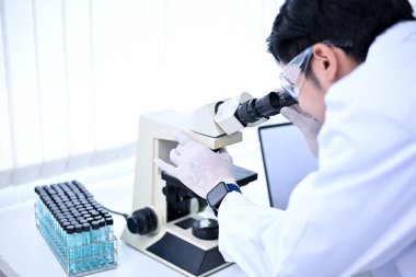 Mikroskop altında virüs örneklerini test edip analiz eden Asyalı zeki bir bilim adamı. Eczacılık, İlaç Konsepti