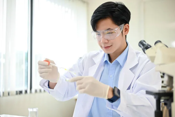 スマートかつ才能のある若いアジアの男性科学者は 彼の科学研究室でペトリ皿にウイルスサンプルを集中調整します — ストック写真